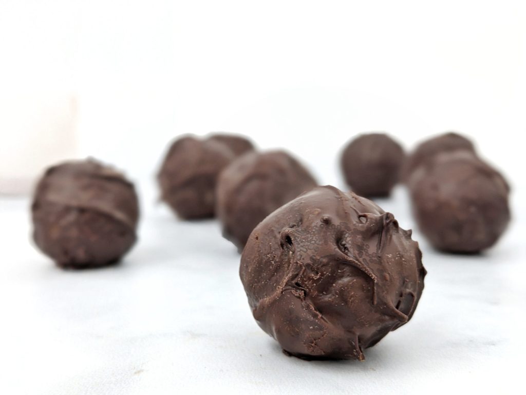 5 Ingredient Chocolate Protein Truffles made with oat flour, cacao powder, protein powder and milk, and dipped in melted chocolate; These no bake protein truffles taste just like brownie balls, and are great for a snack, dessert, or high protein post workout treat!